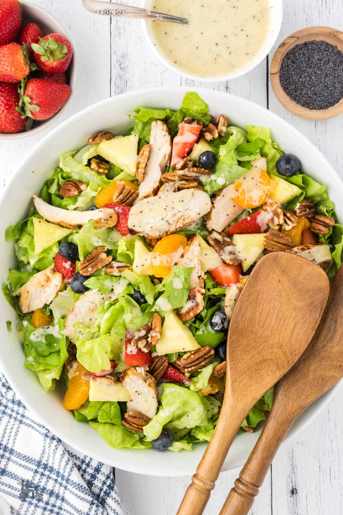 Salad bowl with wooden serving spoons filled with the strawberry grilled chicken breast salad with poppyseed dressing. 