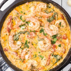 Garlic butter Tuscan Shrimp with Spinach and sun-dried red peppers cooked in a black iron skillet.