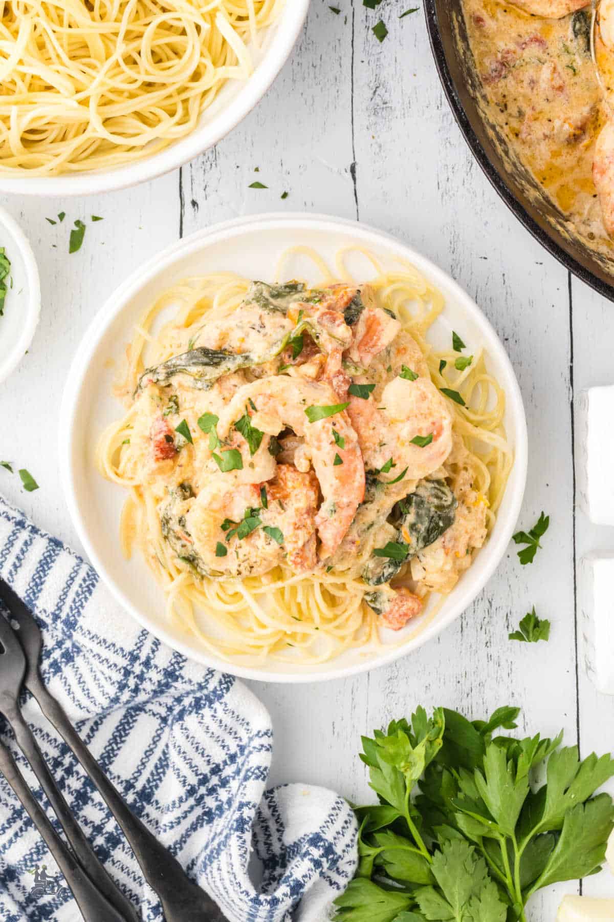 A white plate filled with Tuscan Shrimp Pasta sprinkled with chopped parsley. 