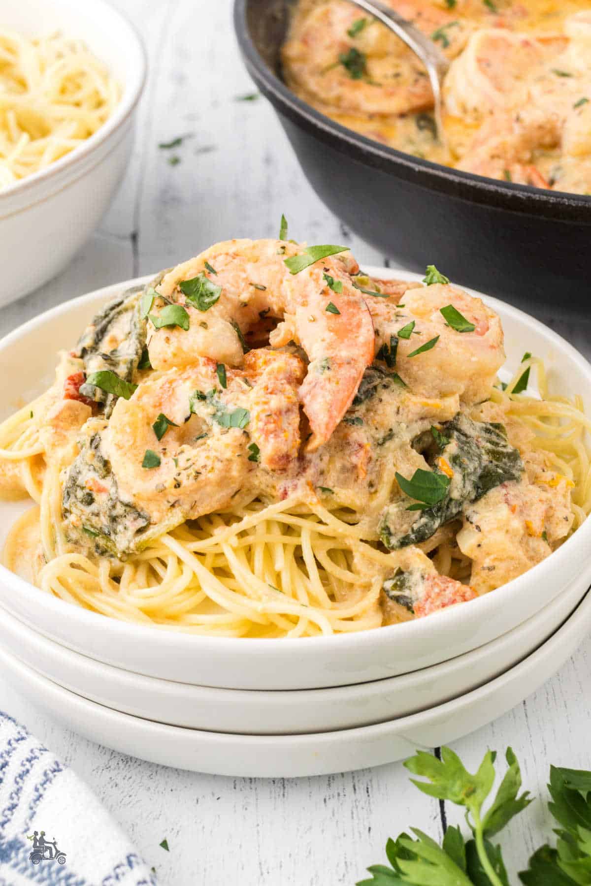 Spaghetti is served with creamy Tuscan shrimp garnished with chopped parsley.
