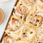 Pinterest image with title overlay features a cinnamon yeast rolls with cream cheese frosting in a large baking dish.