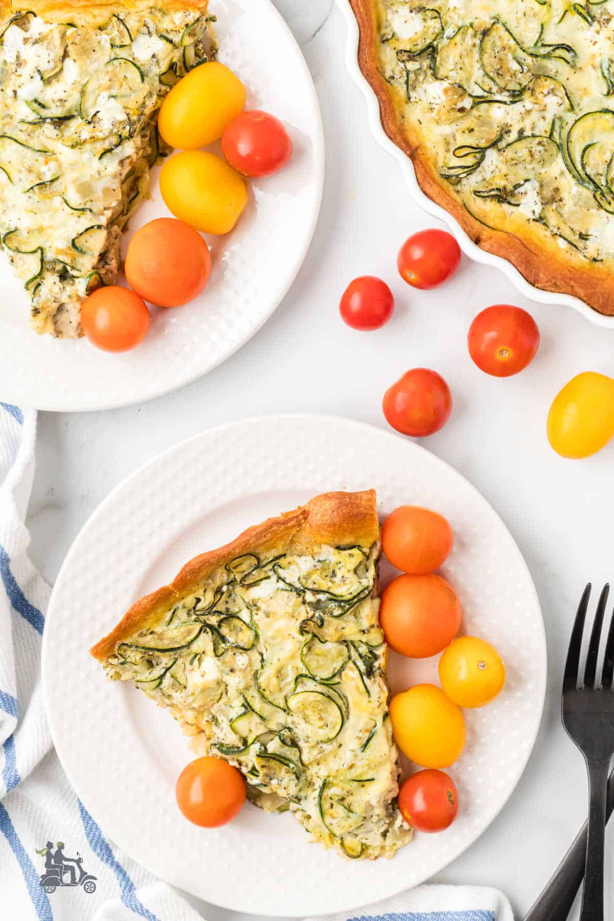 Two slices of zucchini quiche on white plates with colored cherry tomatoes on the side. 