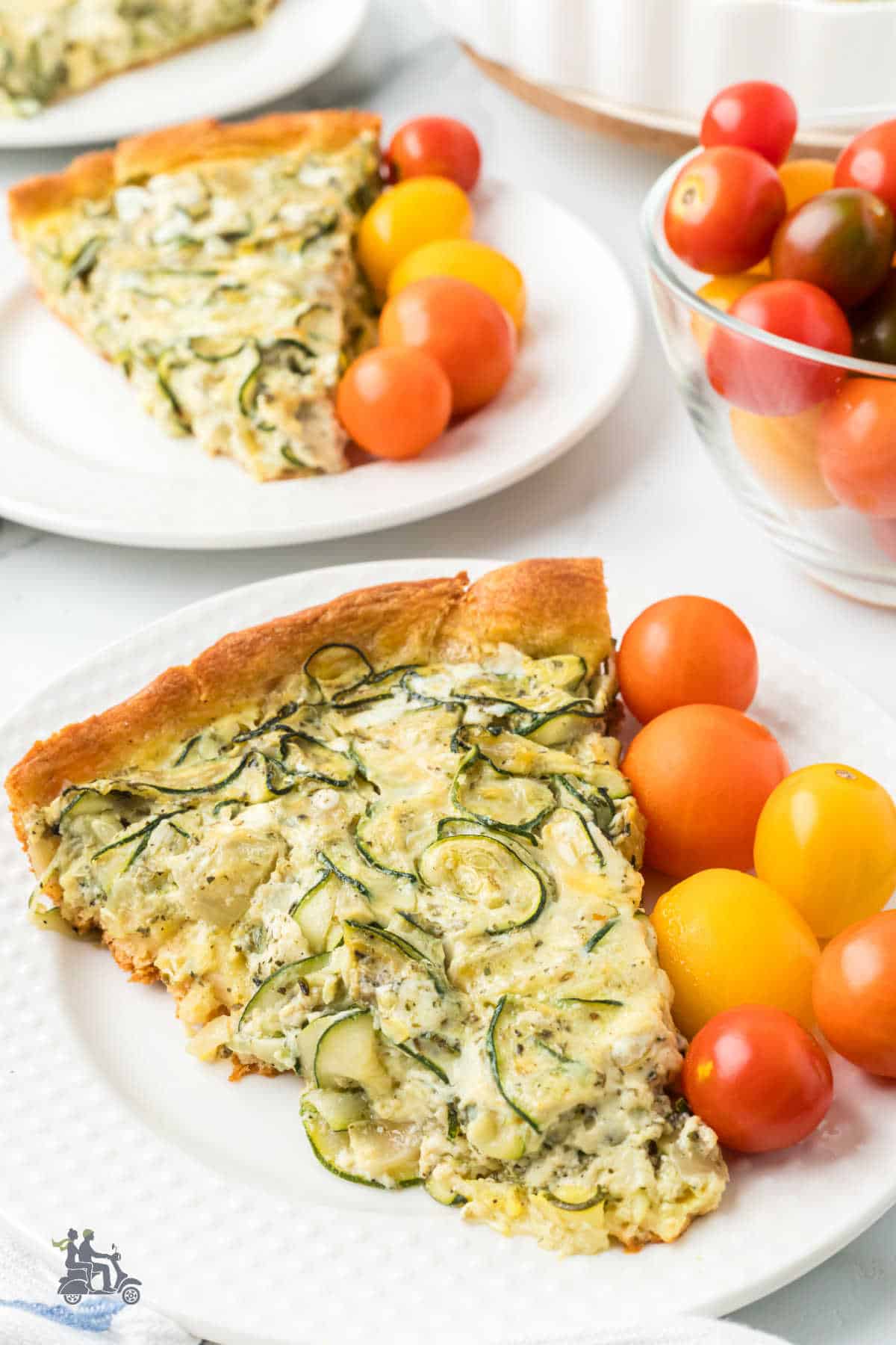 Two slices of Italian Zucchini Crescent Quiche on white plates with orange and red cherry tomatoes on the plate. 