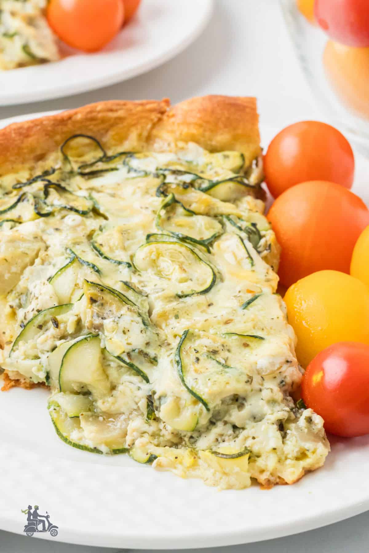 Closeup of a serving of zucchini pie with cherry tomatoes on the side. 