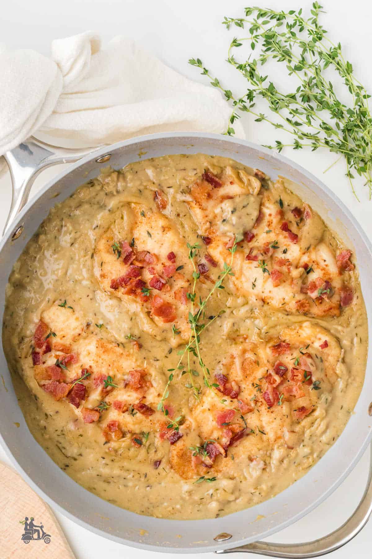 Chicken breasts in a skillet with creamy gravy covering them and bacon pieces sprinkled on top. 