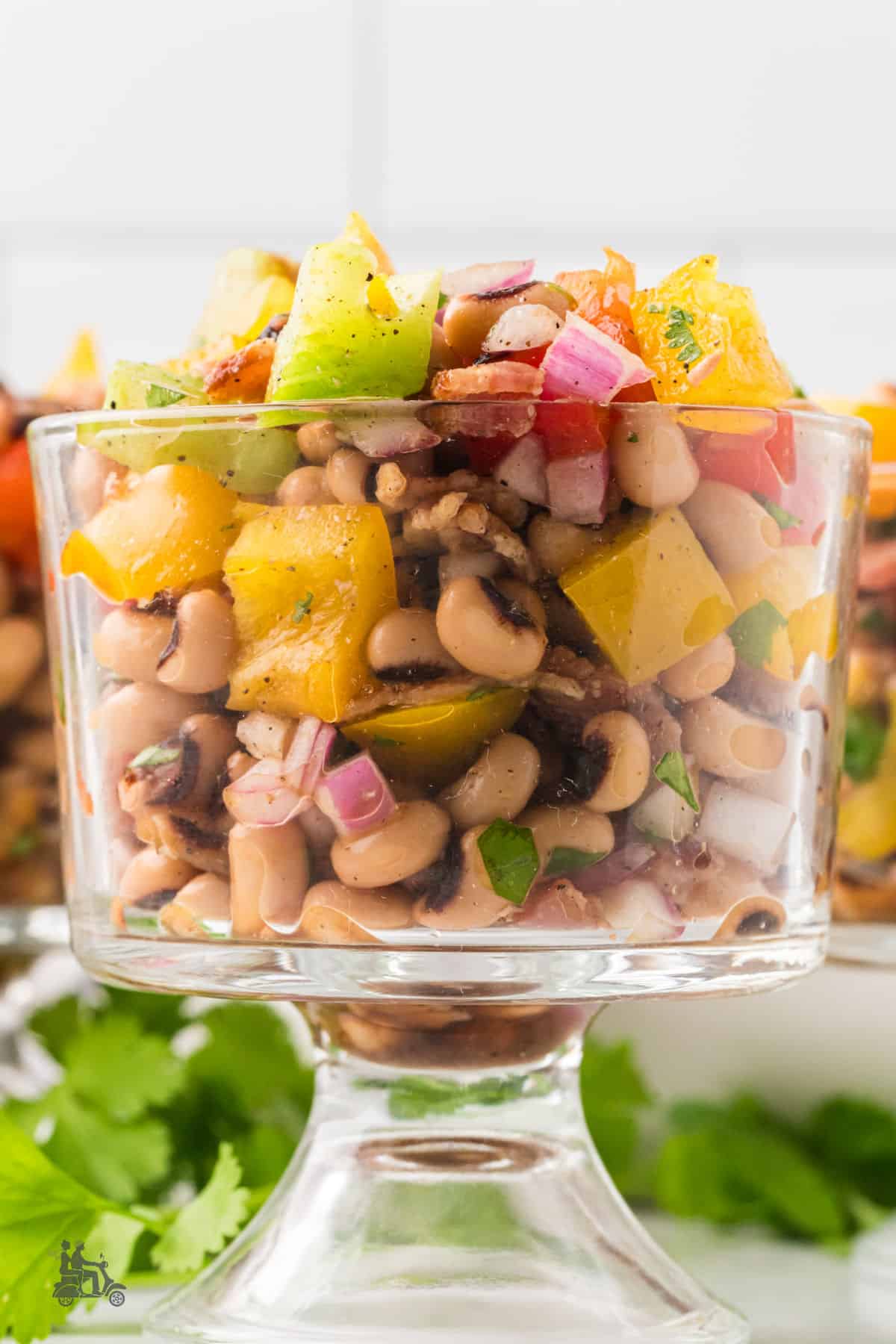 Bean salad made with black-eye peas is placed in a clear glass-footed serving bowl. 
