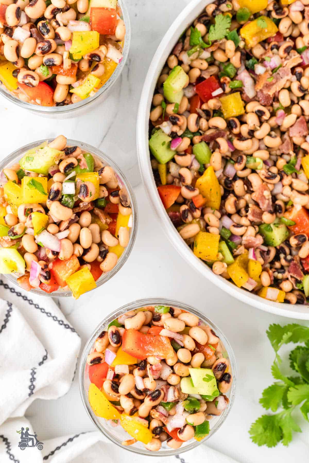 Bowl of black eye peas marinated with peppers and surrounded by three smaller bowls of the salad dish. 