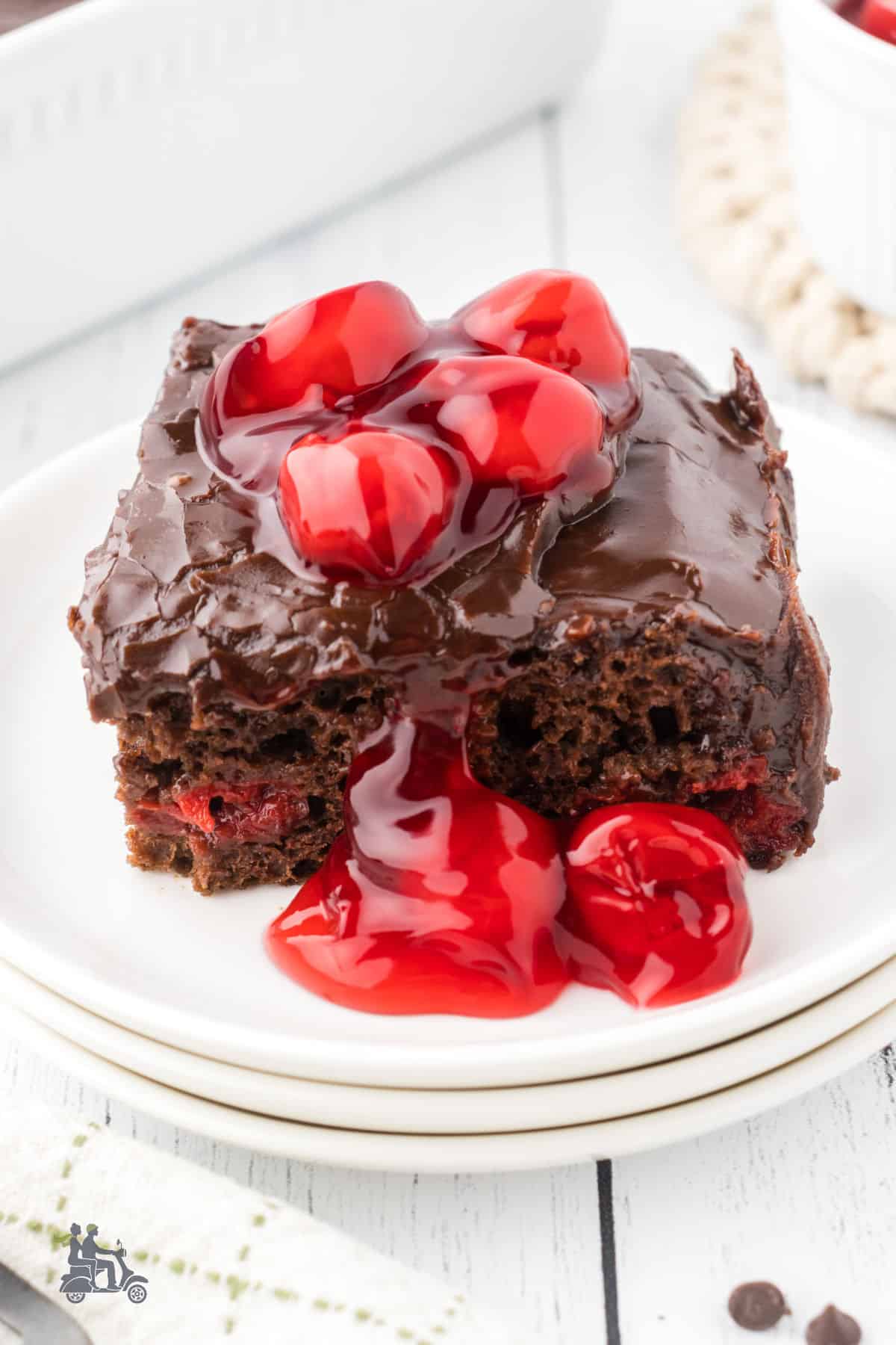 A square of cherry chocolate cake with cherry and sauce on top. 