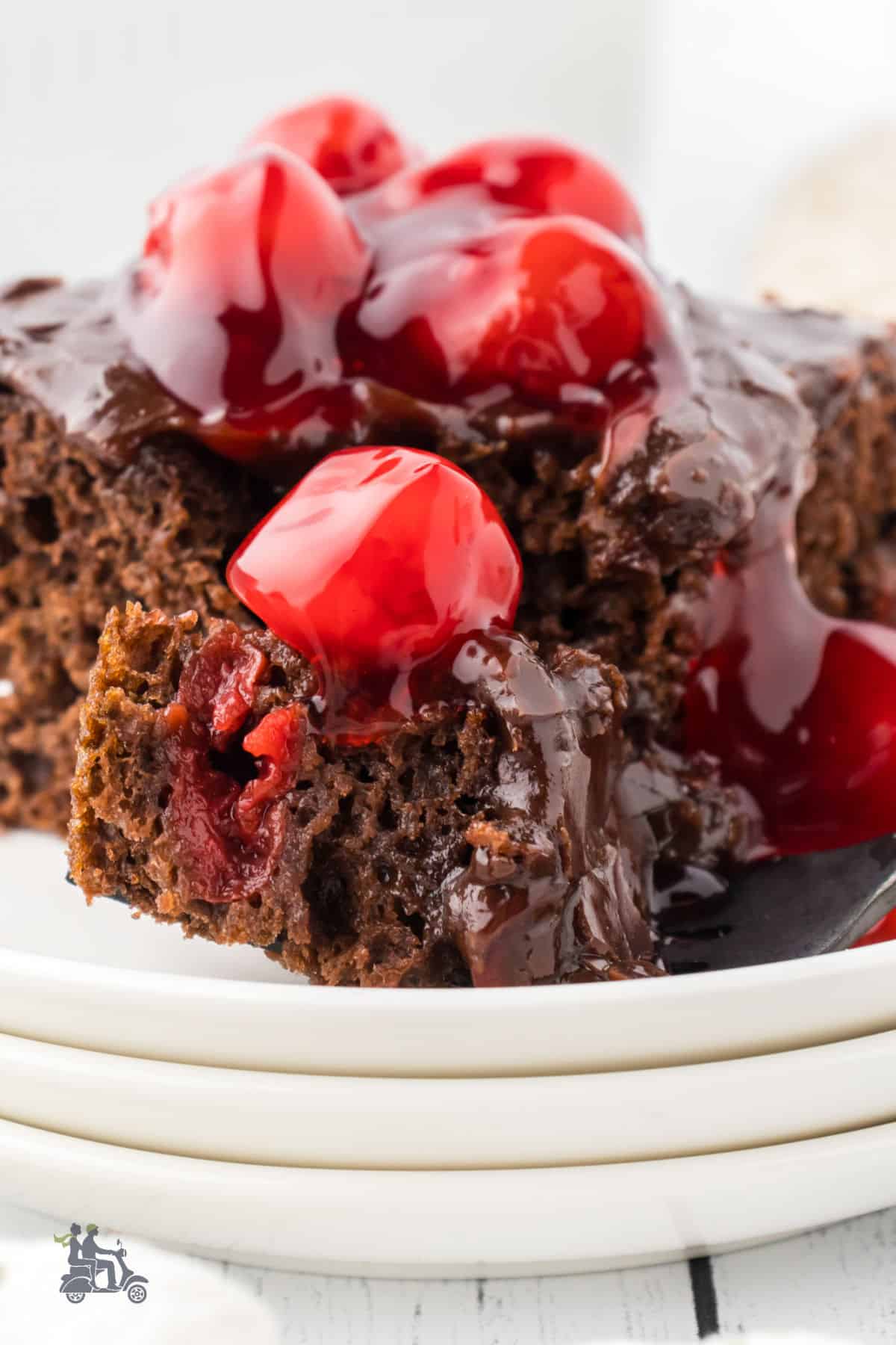 A serving of chocolate cake with cherries on a white plate with a fork on the side. 