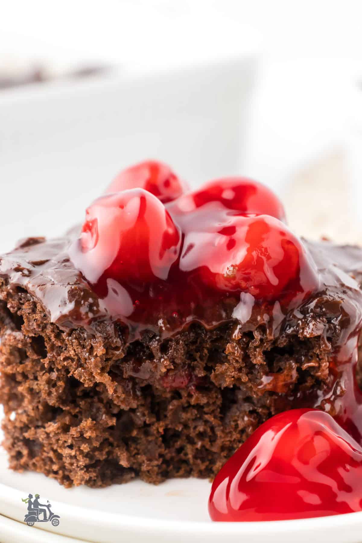 Closeup of a cut square of cherry chocolate cake with cherry pie filling on top. 