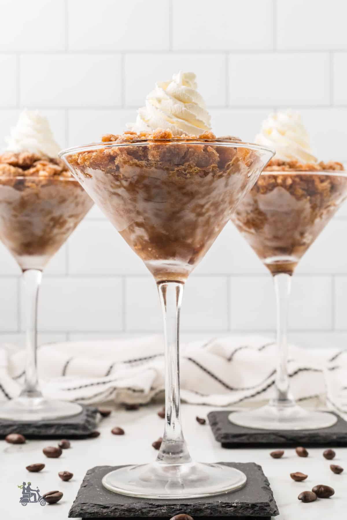 Three stemmed glasses filled with frozen coffee granita topped with sweetened whipped cream.
