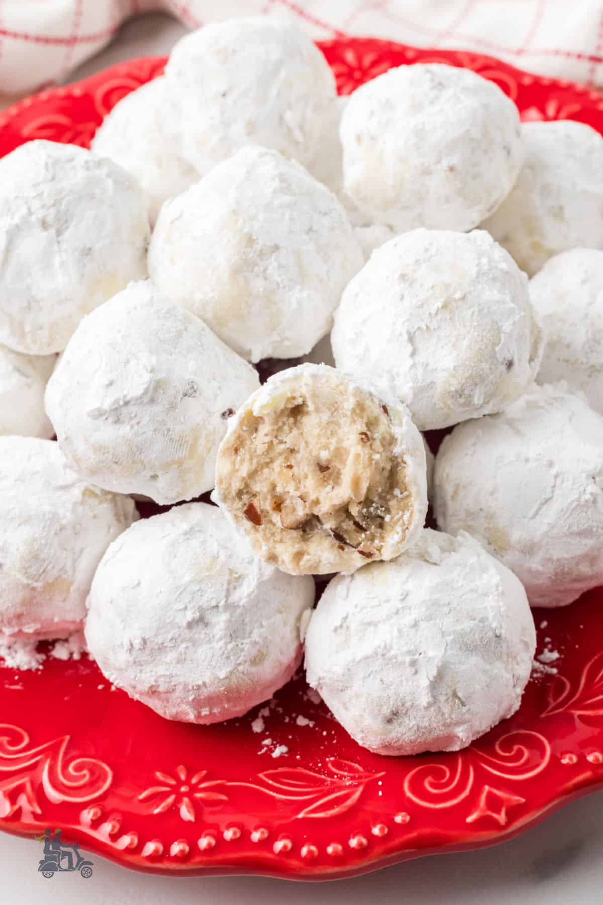 A red cookie plate stacked with snowball cookies and one cookie split in half so the inside is visible. 