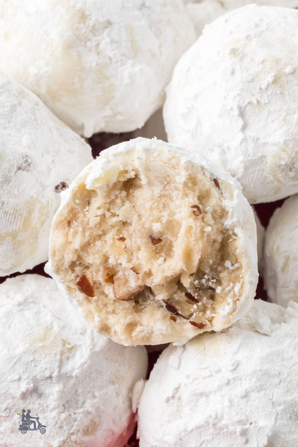 Italian wedding cookies are piled on each other, with one cookie split in half so that the nutty inside is visible. 