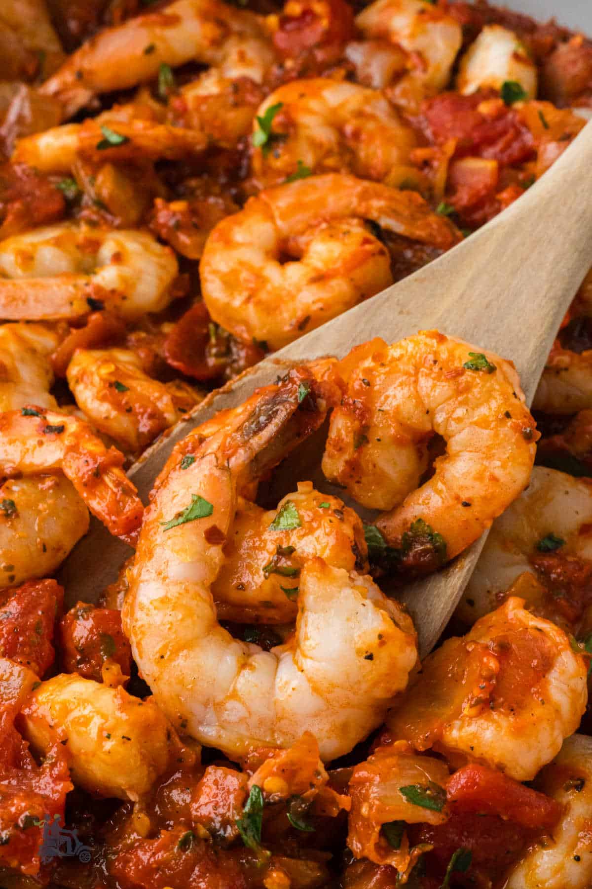 A closeup of a wooden spoon scooping up some of the fra diavolo shrimp.