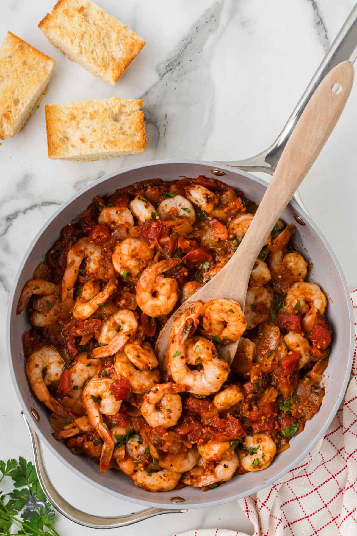 A skillet filled with the shrimp fra diavolo recipe and a wooden spoon removing a spoonful. 