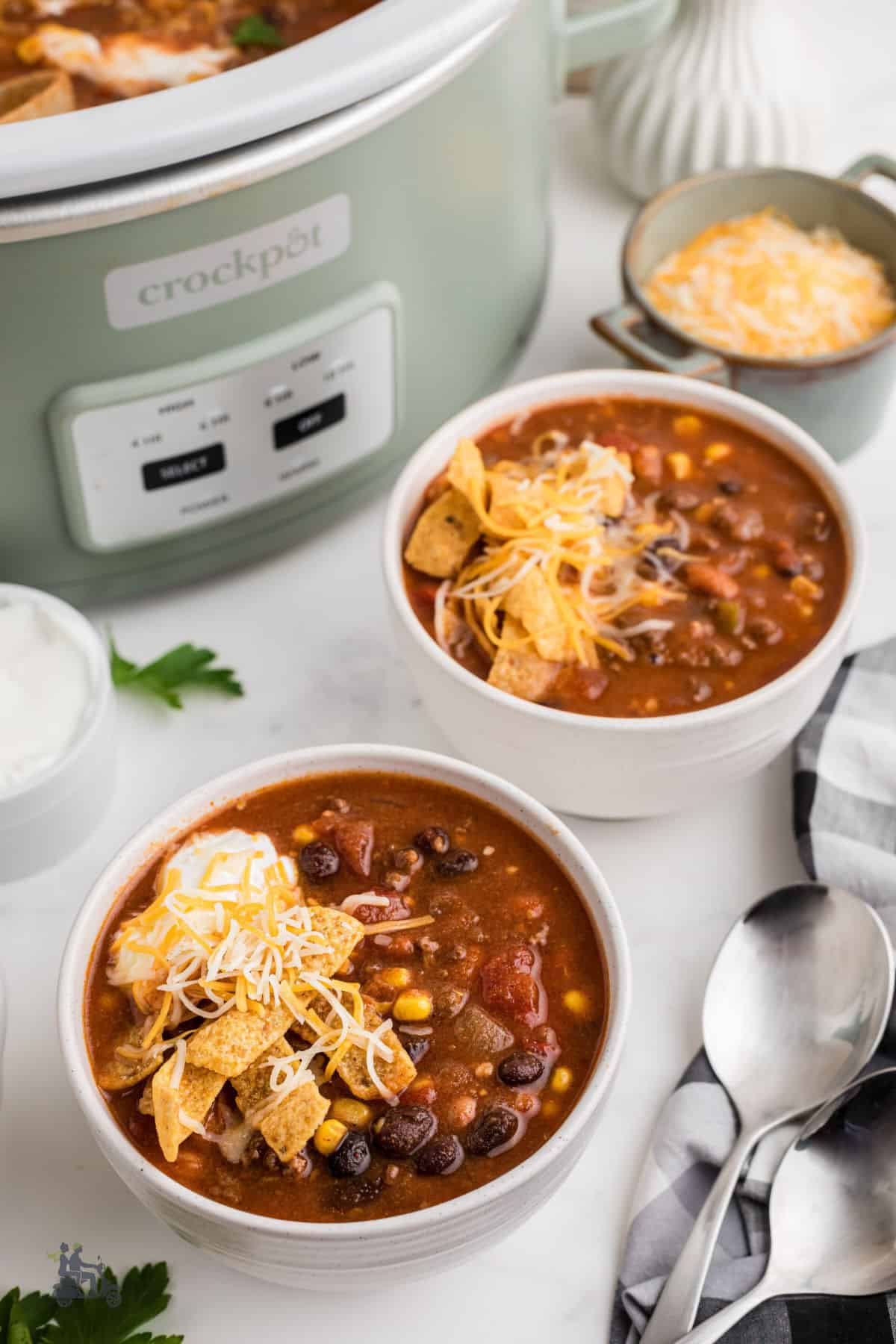 Bowls of Taco Soup garnished with corn chips, sour cream, and shredded cheddar cheese. 