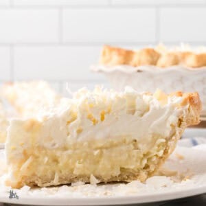 A slice of Triple Cream Pie on a white plate with the full pie in the background.