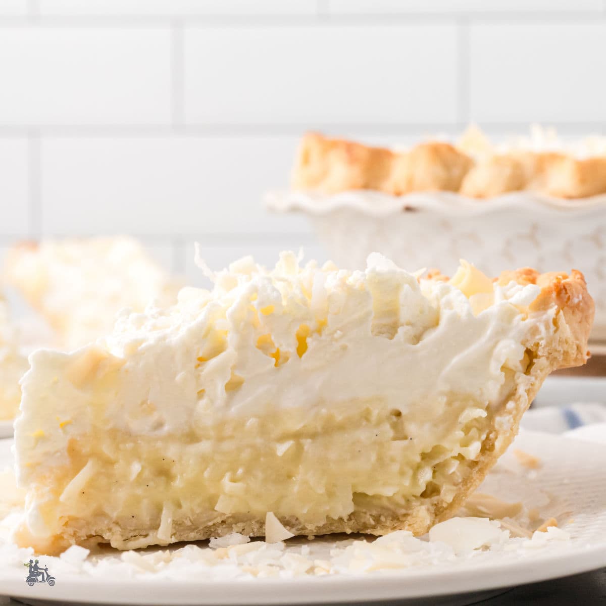 A slice of Triple Cream Pie on a white plate with the full pie in the background.