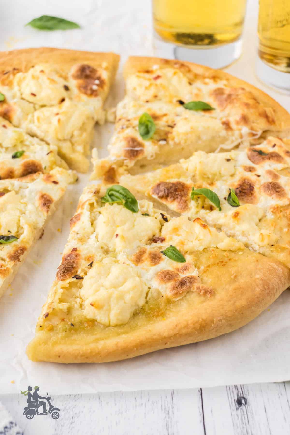 A close view of white pizza made with three cheeses and topped with basil leaves. 