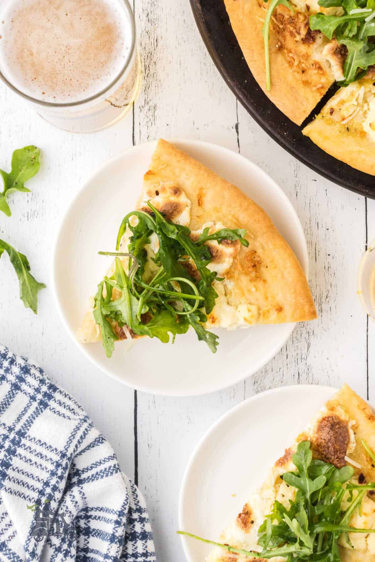 Two slices of white pizza with arugula sprinkled over the slices. 