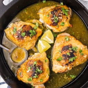 Four chicken thighs in a black iron skillet marinated in honey garlic lime sauce.