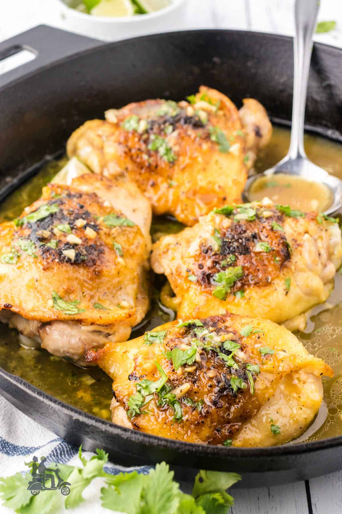 A black cast iron skillet holds the four garlic-lime marinated and baked chicken thighs topped with chopped cilantro. 