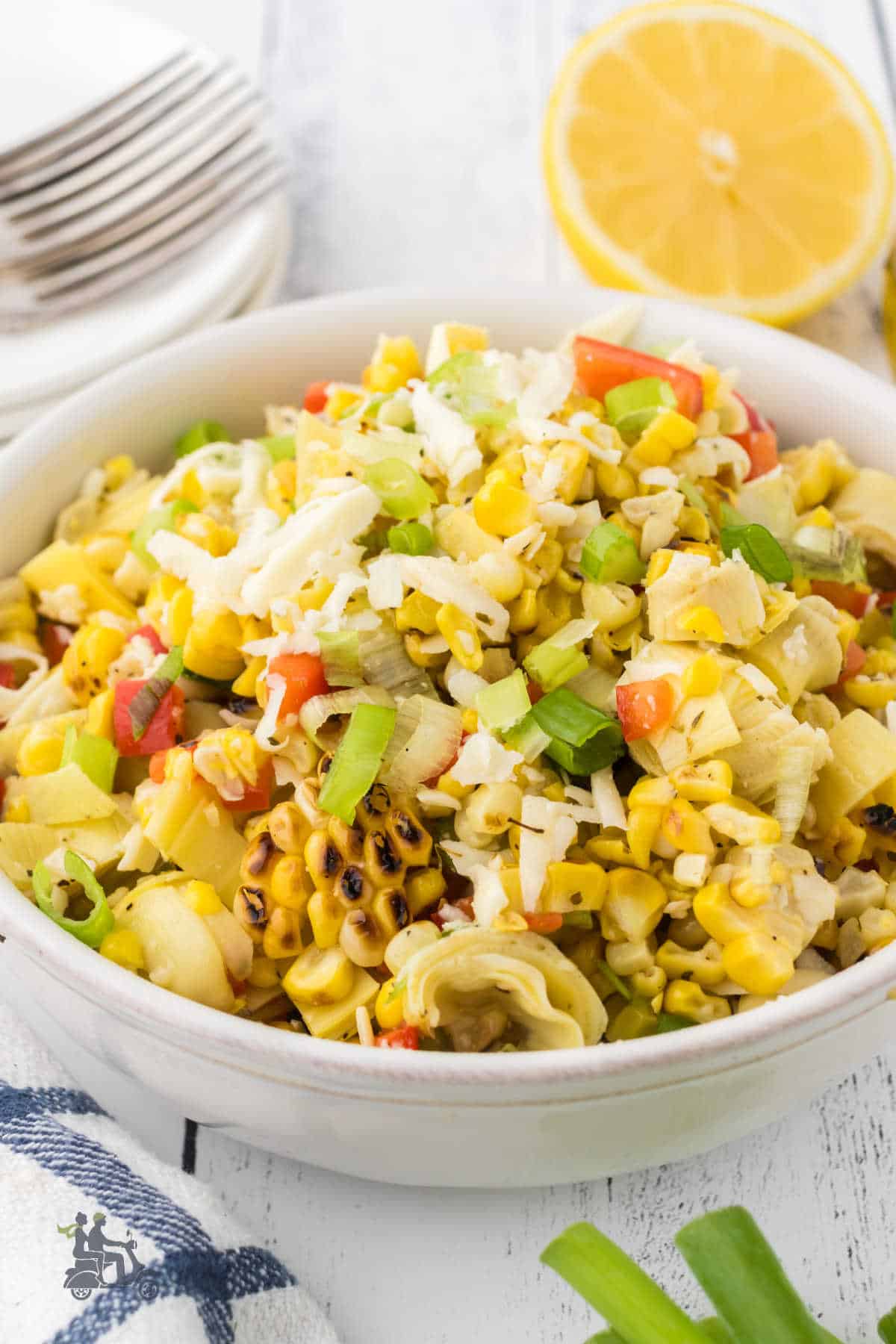 Italian Corn Salad piled into a white serving bowl with a halved lemon on the side.