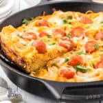 A black cast iron skillet is the baking form used to make the spaghetti frittata with grape tomatoes on top.