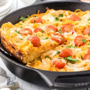 A black cast iron skillet is the baking form used to make the spaghetti frittata with grape tomatoes on top.