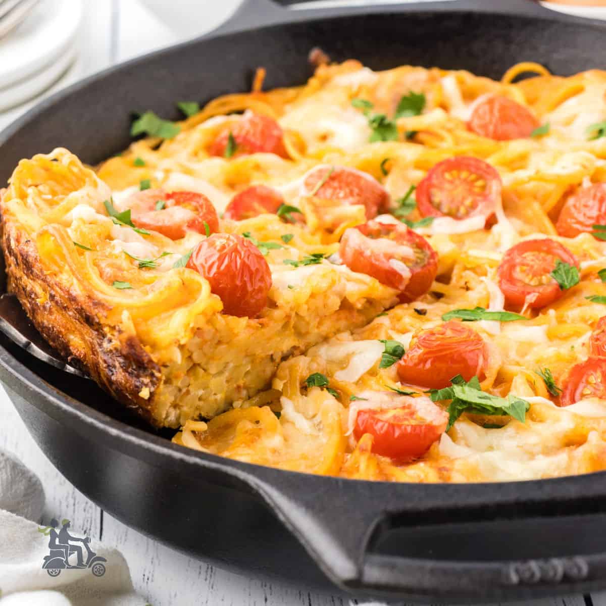 A black cast iron skillet is the baking form used to make the spaghetti frittata with grape tomatoes on top.