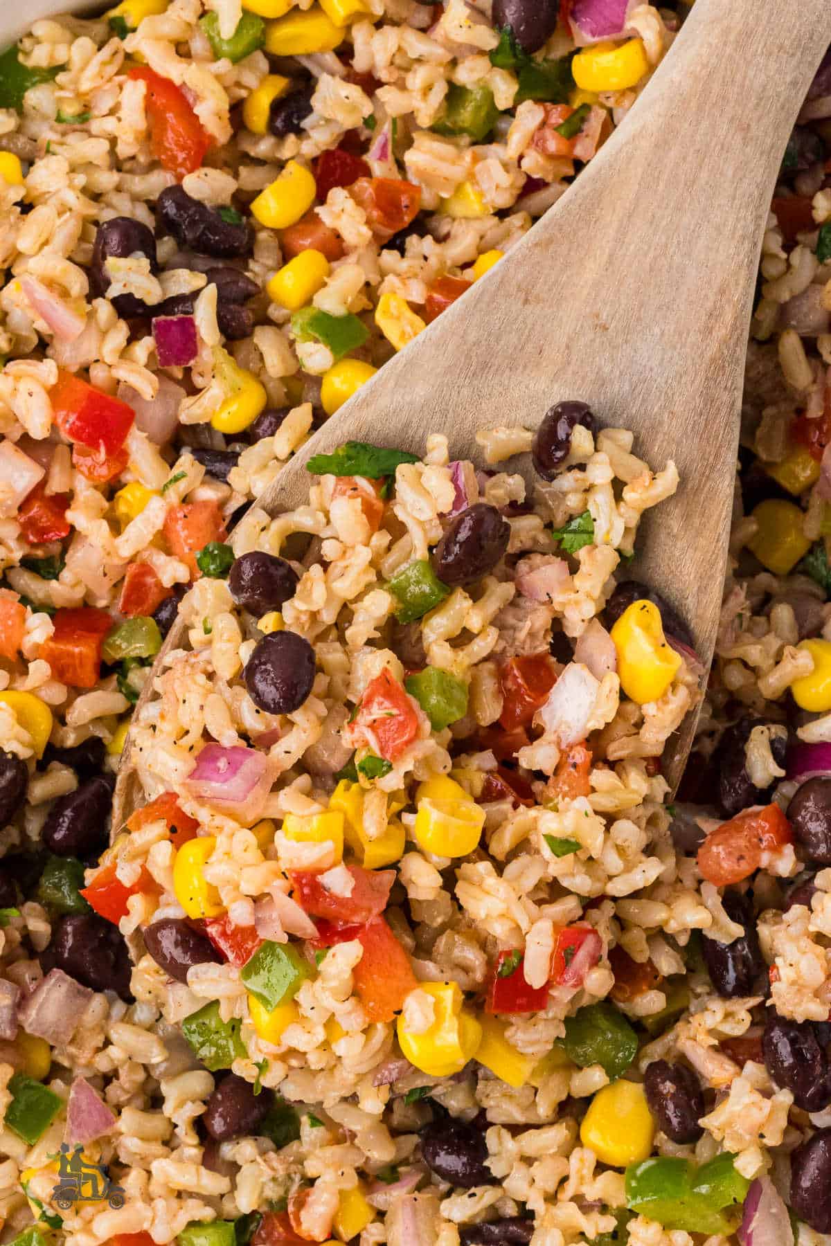 A wooden serving spoon scoops a helping of tuna rice salad. 