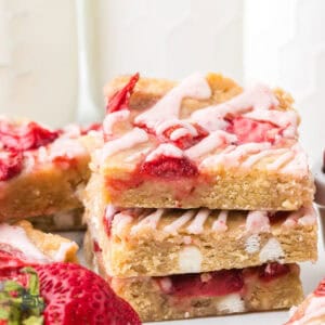 Strawberry White Chocolate Blondies stacked up one on the other with a glass of milk in the background.