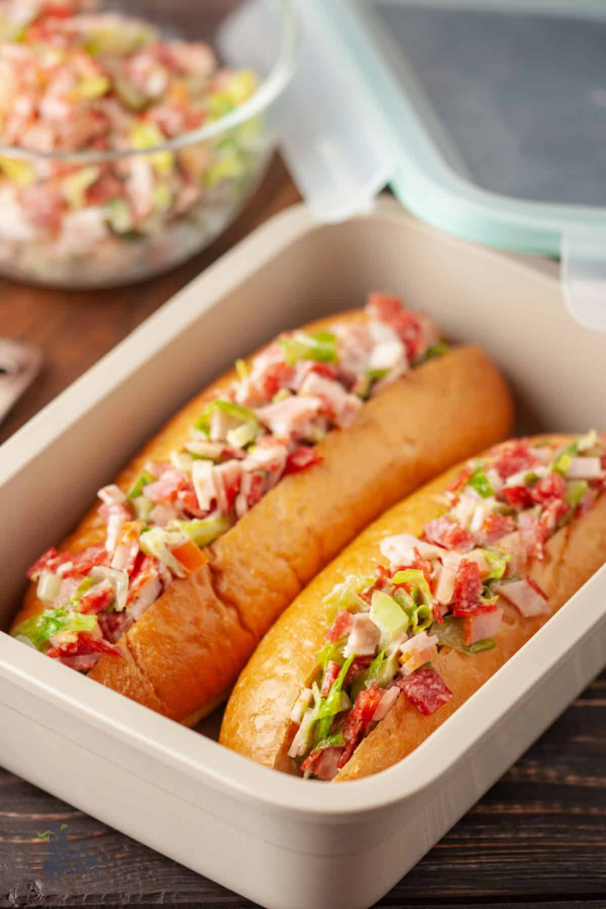 Two Sandwich buns filled with Italian chopped salad in a plastic carry container. 