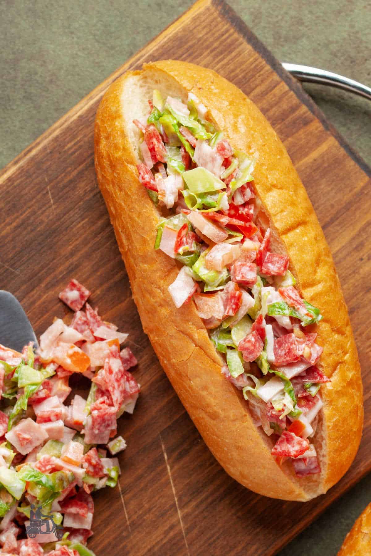 Italian Chopped Salad Sandwich in a sandwich bun on a wooden cutting board. 