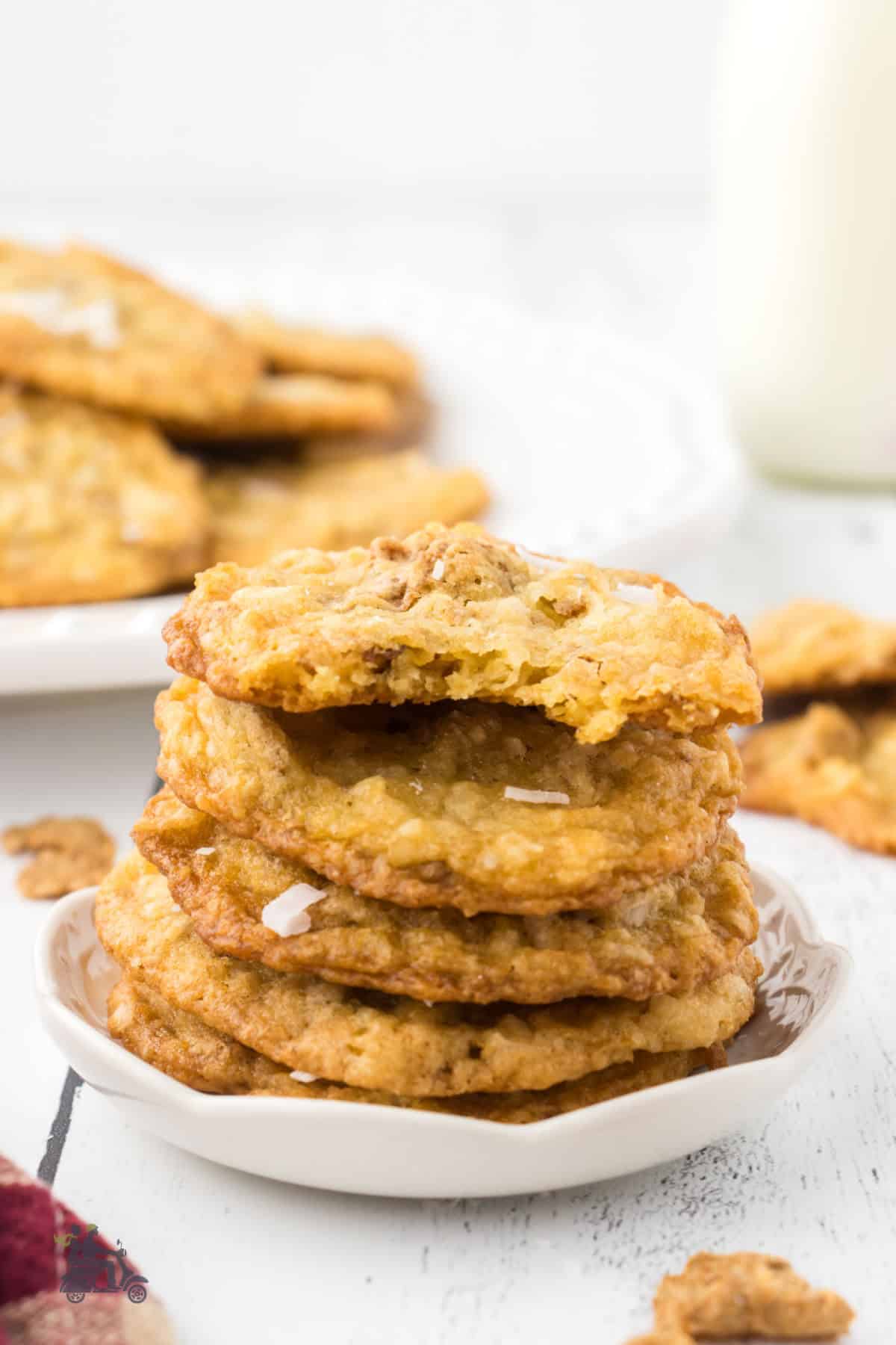 Crispy coconut cookies are piled on a plate with a bite from the top cookie.