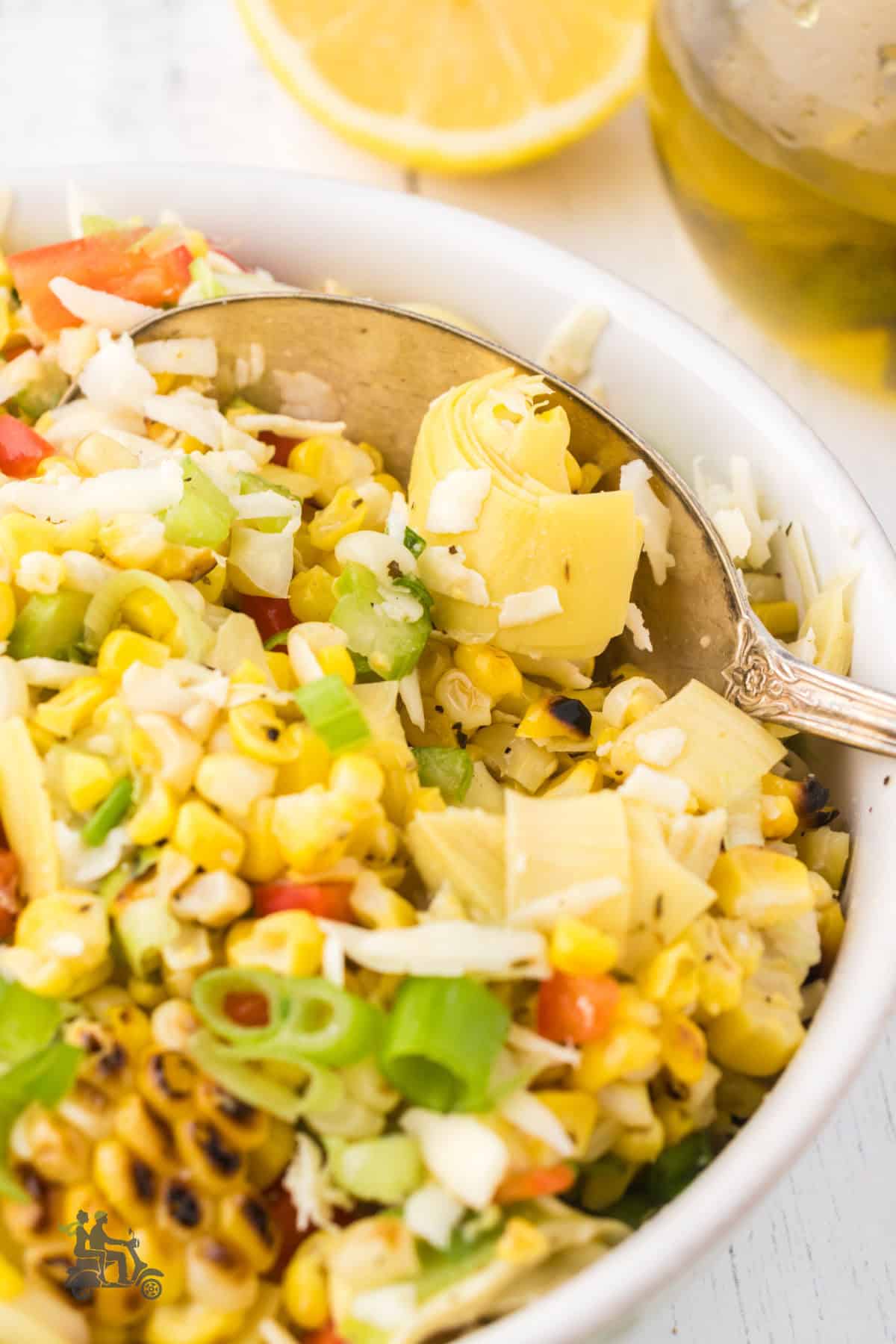A white serving bowl holds the grilled corn salad with artichoke hearts and lemon vinaigrette dressing. 