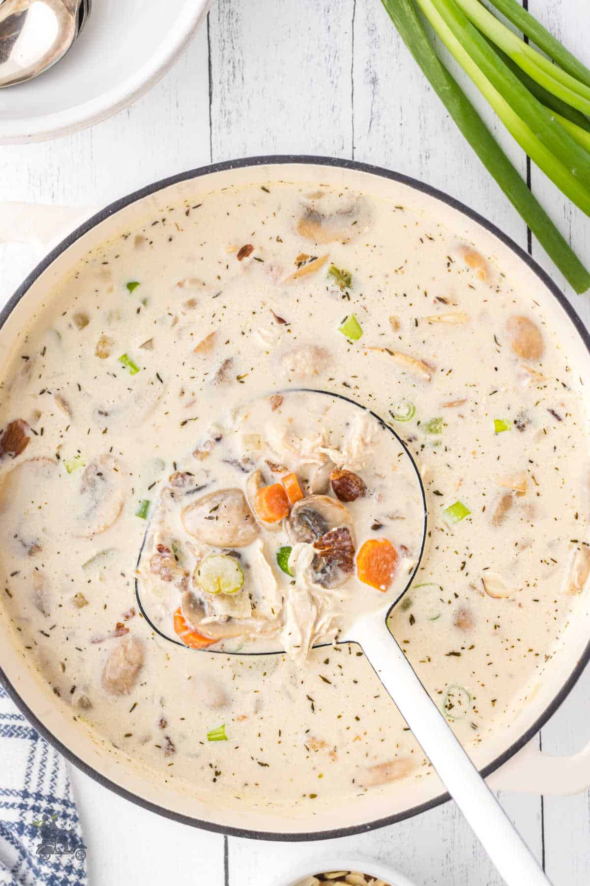 White soup pot filled with creamy mushroom and chicken wild rice soup with a spoon removing a helping.