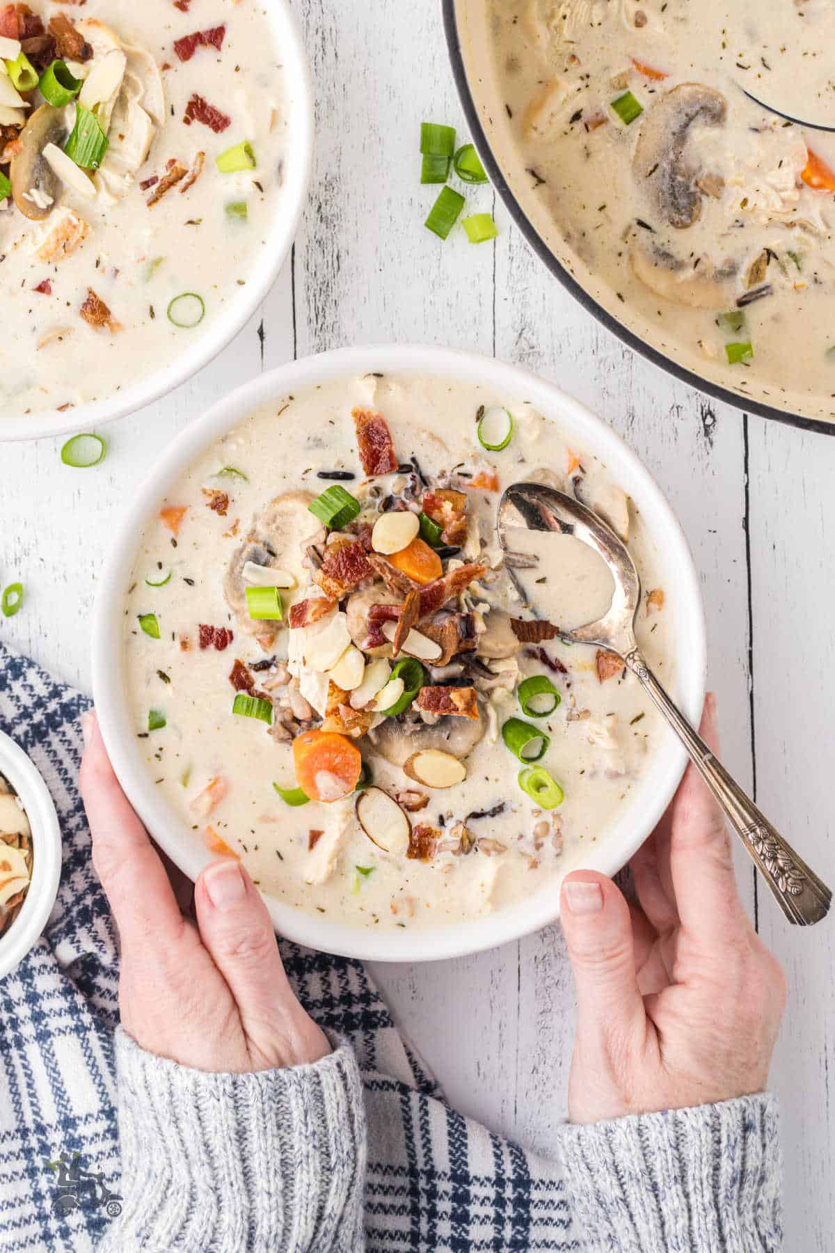 A bowl of Chicken Wild Rice Soup with a pair of hands holding the white bowl.