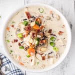 Creamy Chicken Wild Rice Soup recipe served in a white bowl and garnished with onions, bacon, and almonds.