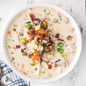 Creamy Chicken Wild Rice Soup recipe served in a white bowl and garnished with onions, bacon, and almonds.