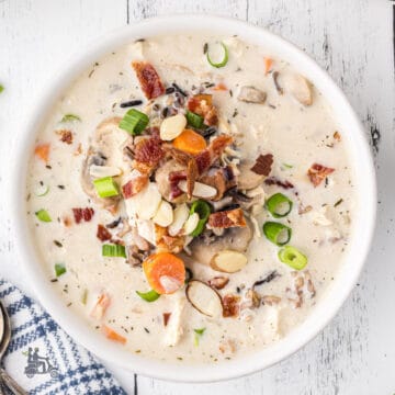 Creamy Chicken Wild Rice Soup recipe served in a white bowl and garnished with onions, bacon, and almonds.