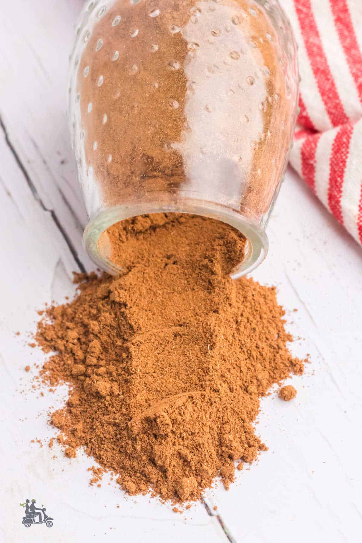 Spice blend for apple pie in a jar with contents spilled on a white wooden table. 