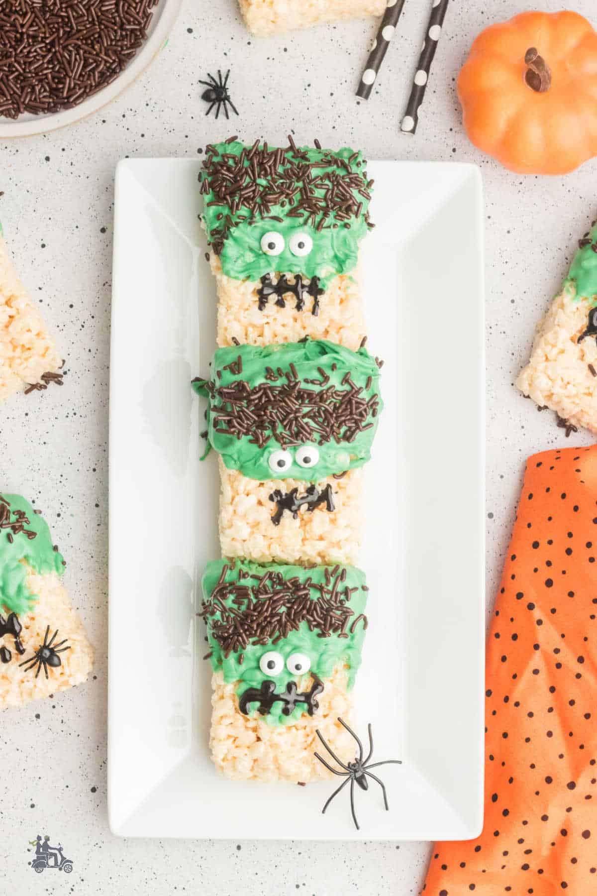 Halloween Rice Krispie Treats decorated as Frankenstein's heads are served on a white rectangular plate. 