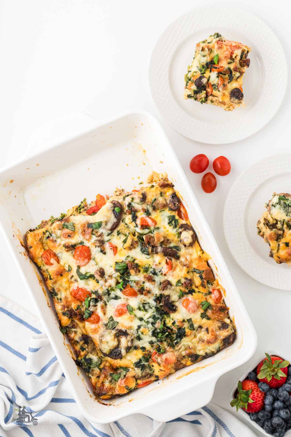 Baking dish with two squares of baked breakfast strata removed and placed on serving plates.