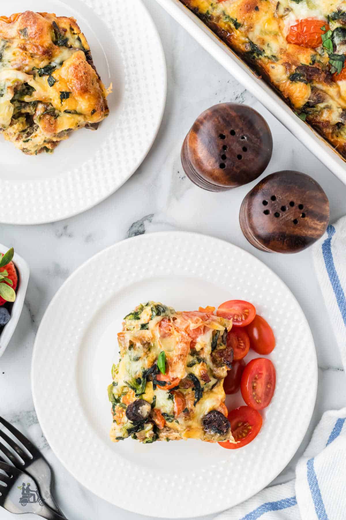 Overhead view of the breakfast strata recipe completed with a serving on a white plate. 