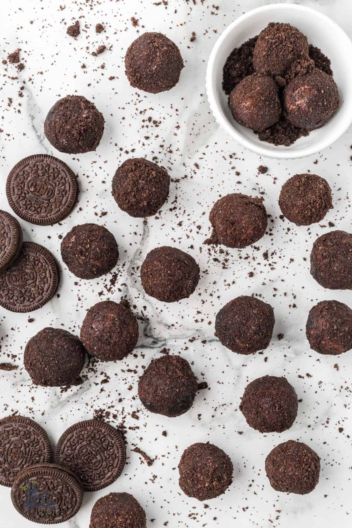 On a white counter, no-bake espresso rum balls are rolled in crushed Oreo cookie crumbles, and more cookie crumbs are scattered. 