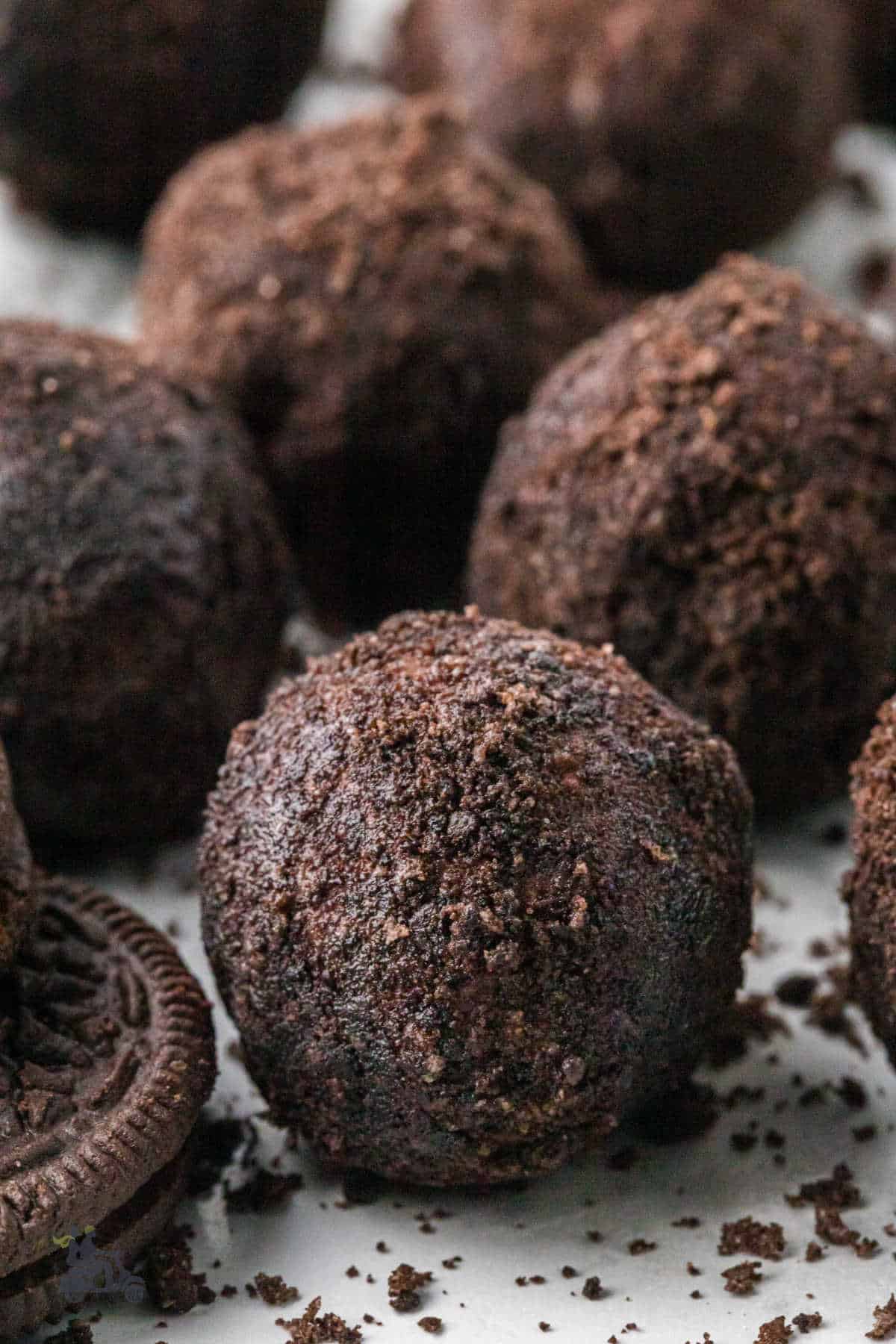 Chocolate cream cheese truffles rolled in crunchy Oreo Cookie crumbs on a white counter. 