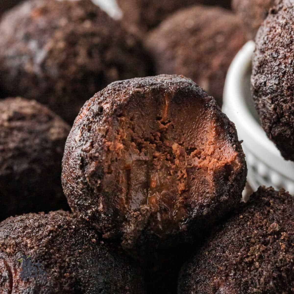 Chocolate rum balls are stacked on each other with a bite mark on the top rum ball.