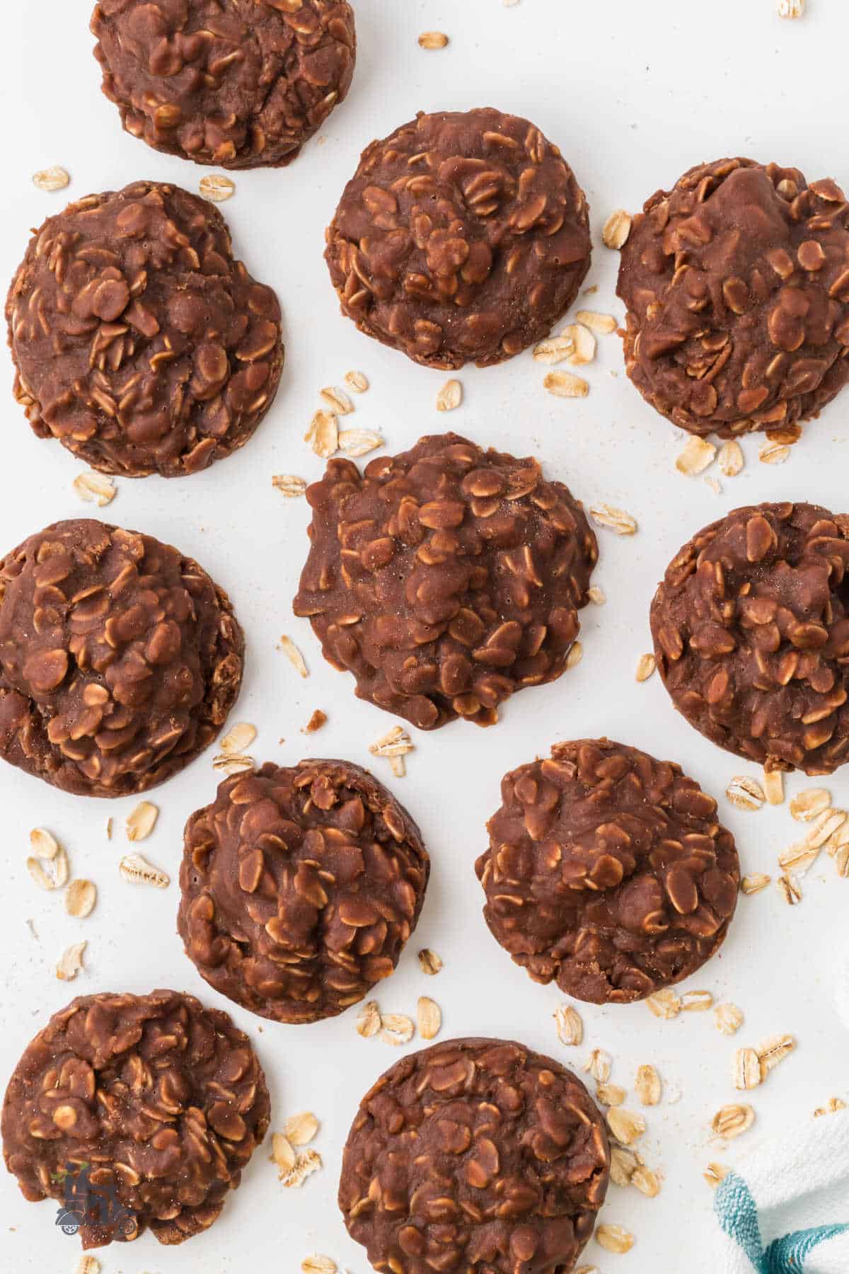 No-bake Chocolate Oatmeal Cookies on a white table surface with oatmeal strewn around the cookies. 