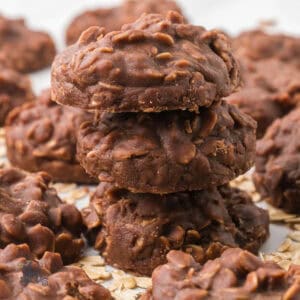 There are three Chocolate Oatmeal Cookies of the no-bake variety on a table, with more cookies surrounding the stack of three.